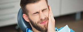 Young man in dental grimacing and holding head